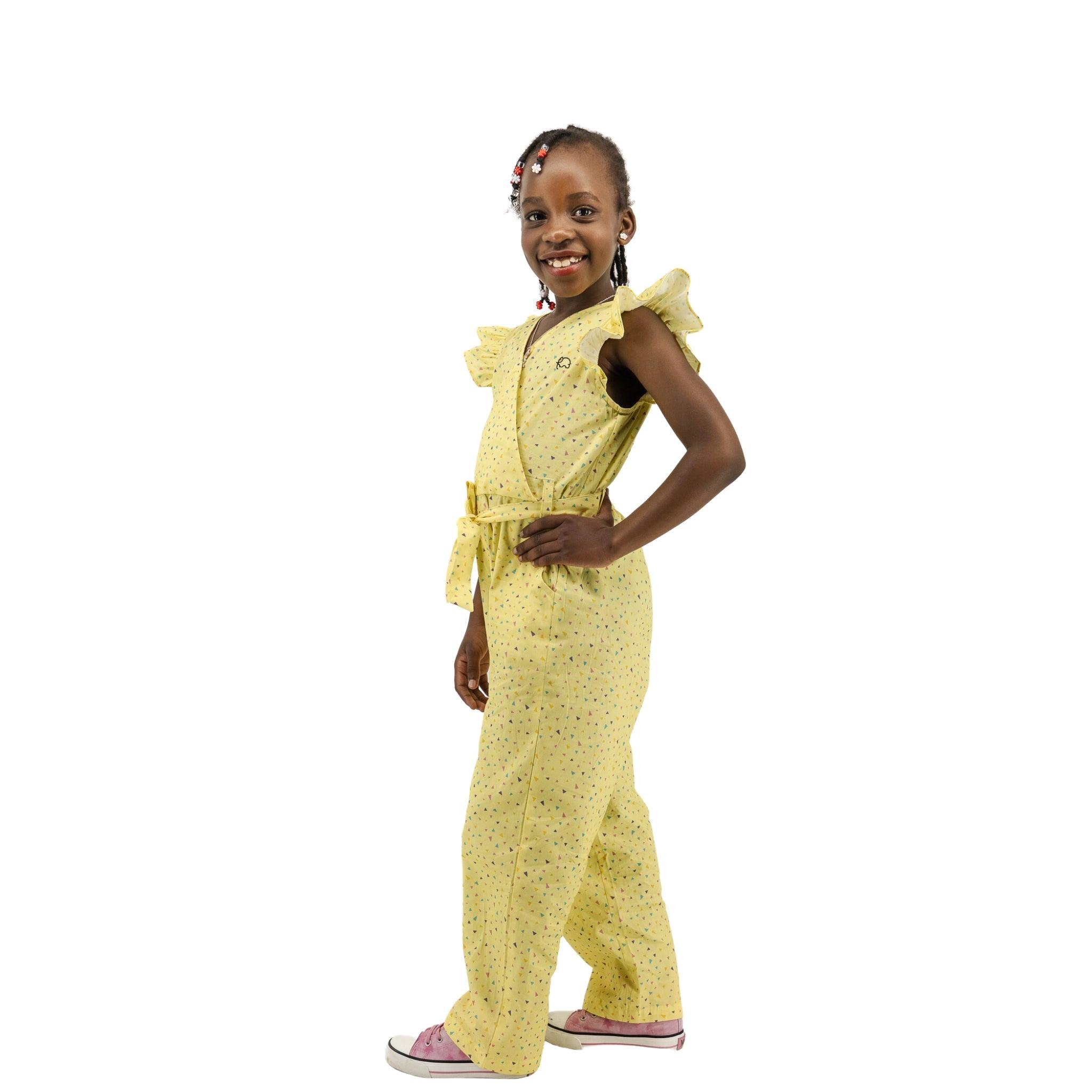 Young girl smiling, standing in a Karee Lemon Meringue Cotton V-Neck Jumpsuit for Girls with her hands on her hips, isolated on a white background.