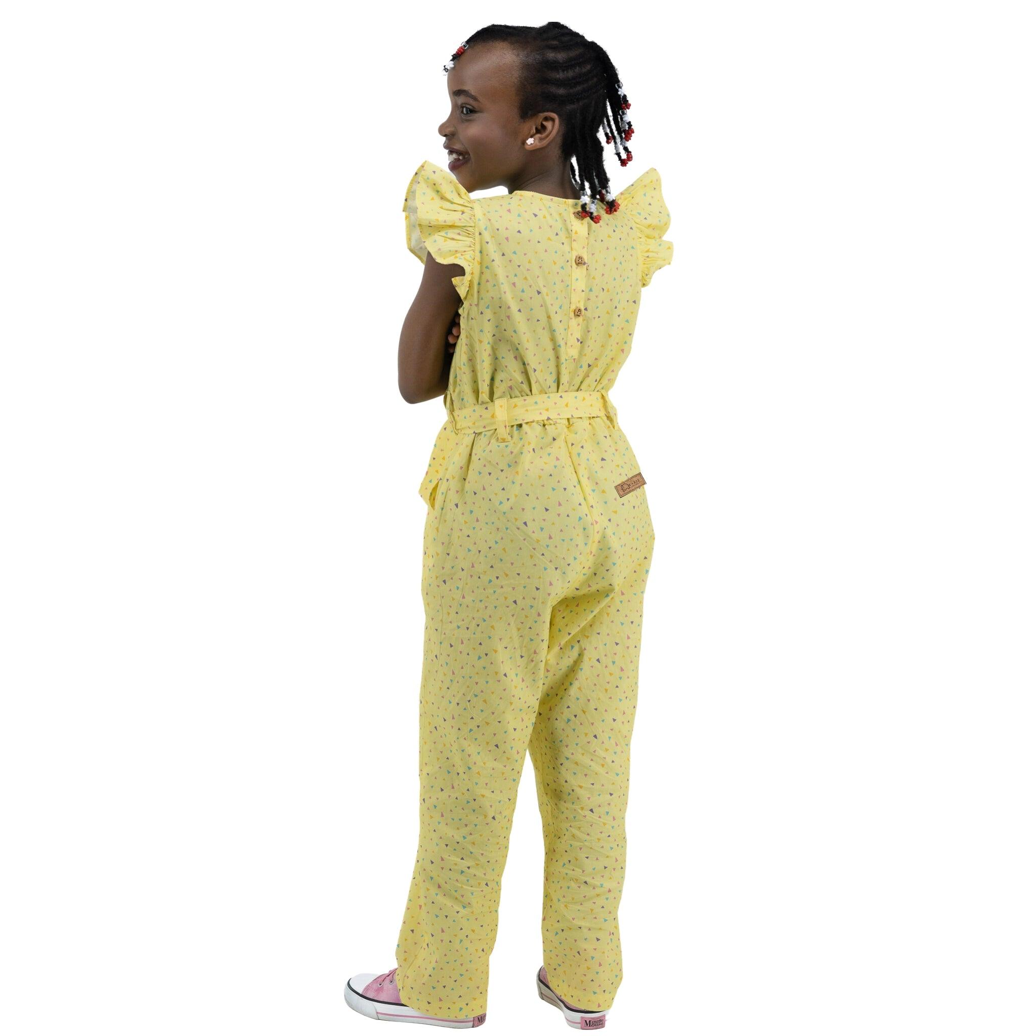 Young girl in a Lemon Meringue Cotton V-Neck Jumpsuit for Girls by Karee looking over her shoulder and smiling, standing against a white background.