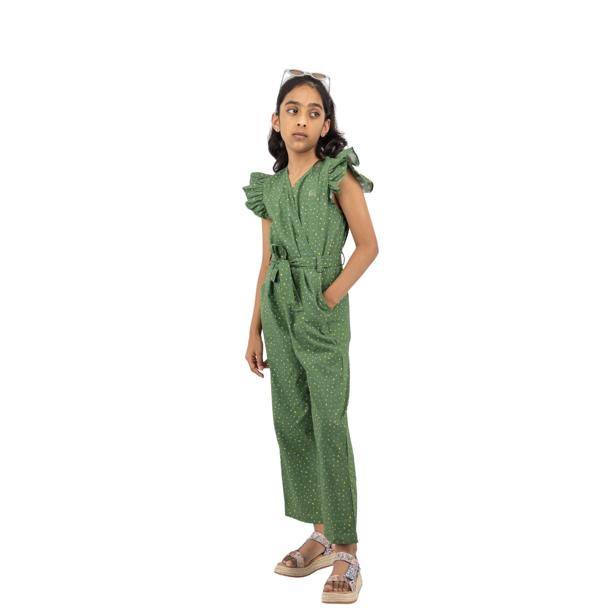 Young girl in a Karee Green Confetti Cotton V-Neck Jumpsuit for Kids with polka dots, wearing sunglasses on her head, standing with one hand on her hip against a white background.