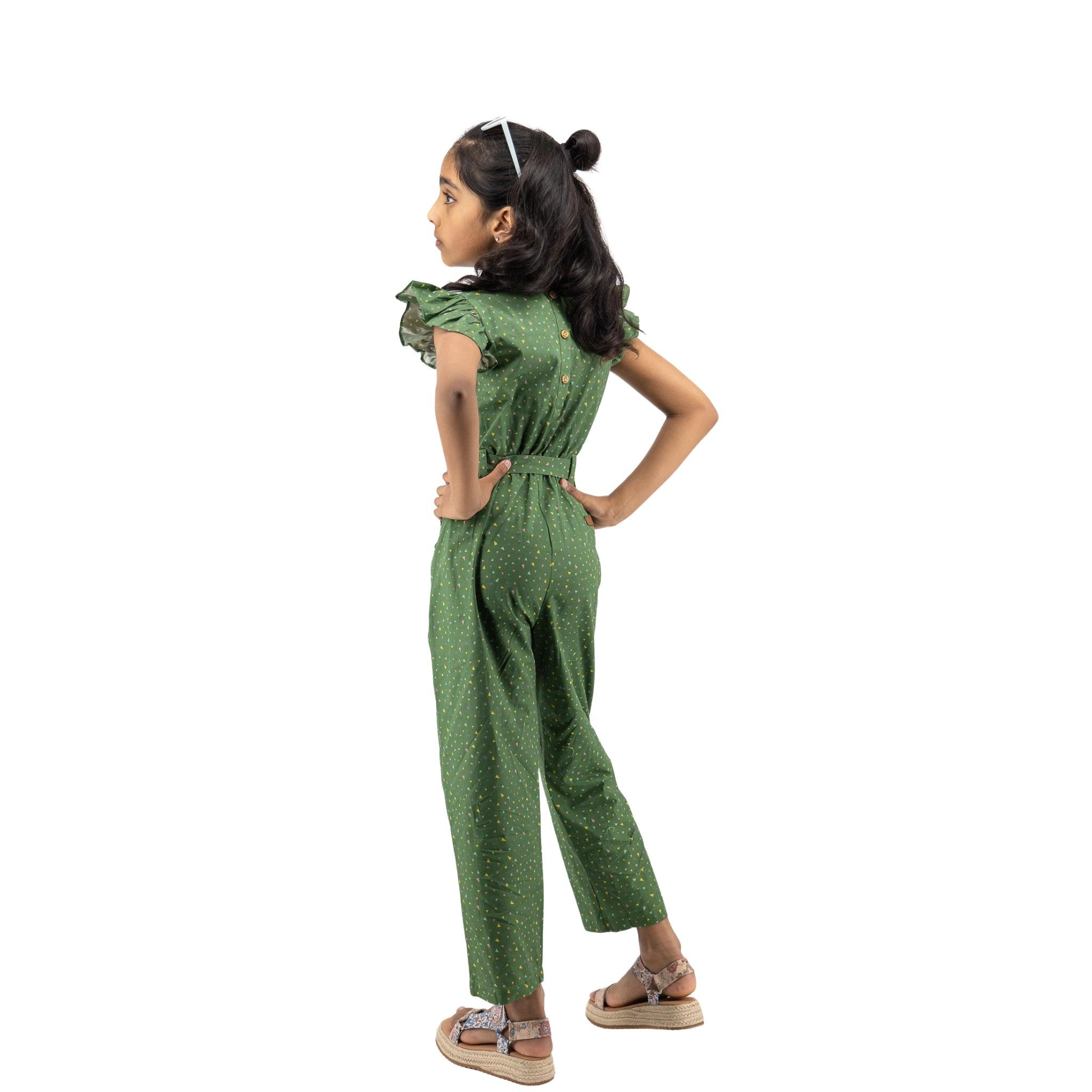 Young girl in a Karee Green Confetti Cotton V-Neck Jumpsuit for Kids, standing sideways with hands on her hips, looking over her shoulder, isolated on white background.