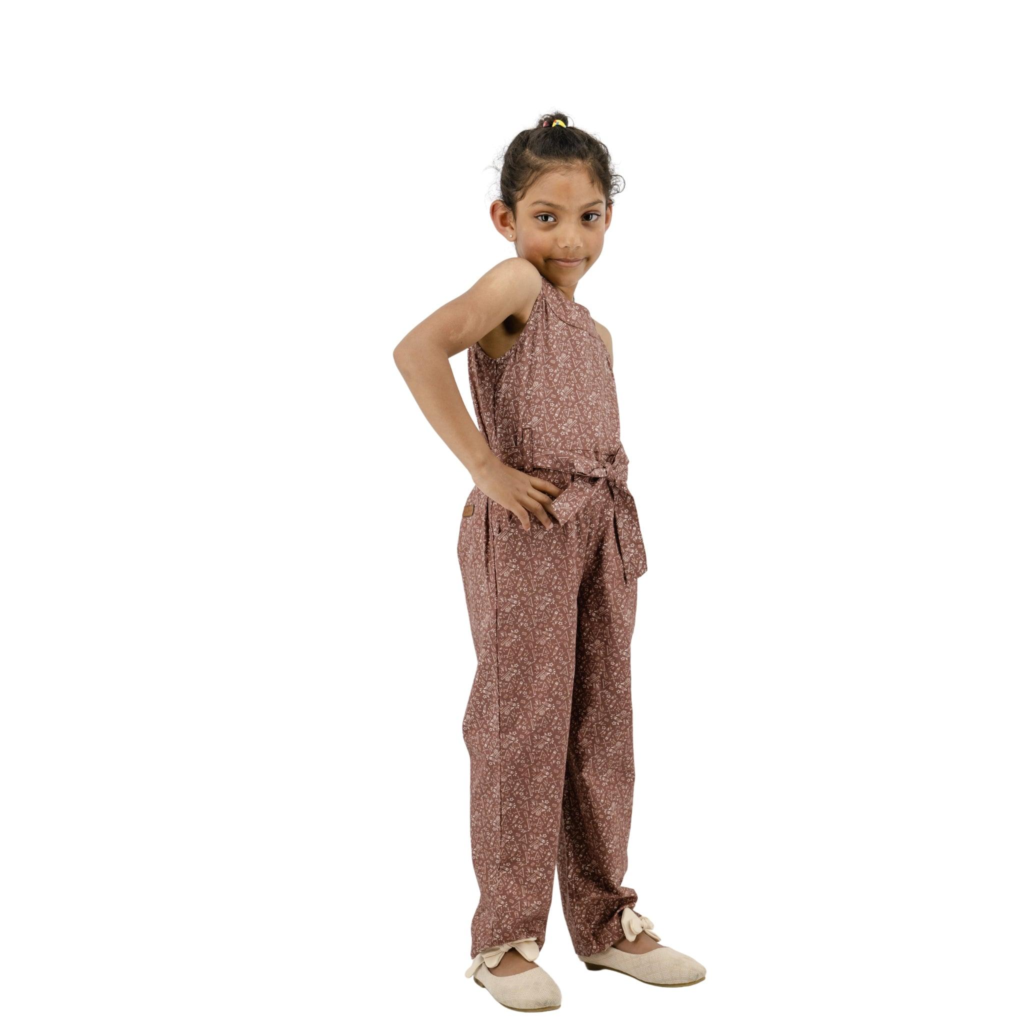 Young girl in a Karee cocoa brown cotton jumpsuit for girls posing with hands on her hips, smiling at the camera against a white background.