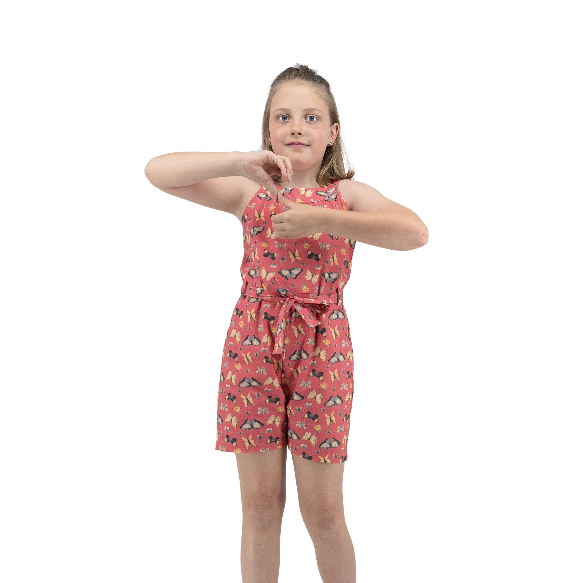 Young girl in a floral Ruby Trek Cotton Romper by Karee making a timeout sign with her hands, standing against a white background.