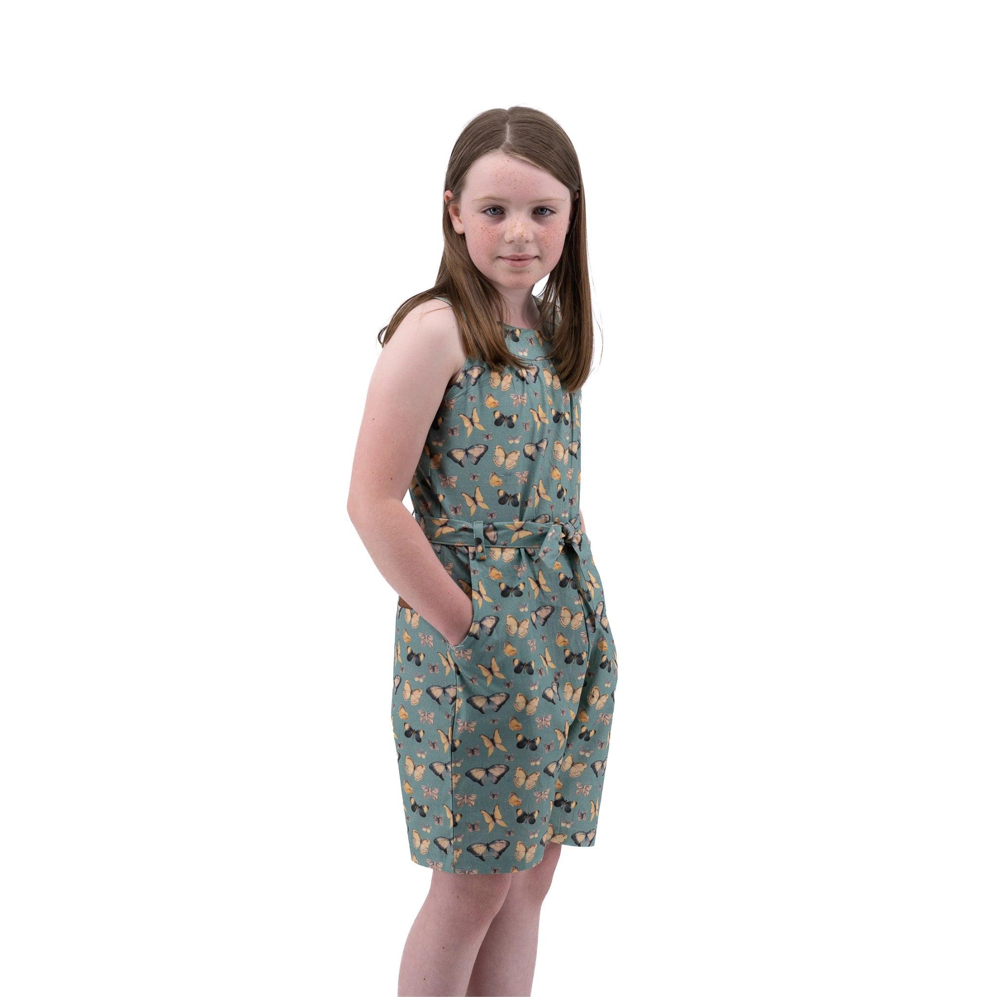 Young girl in a Karee Blue Surf Adventure-ready Cotton Play Suit with butterfly pattern standing against a white background, looking at the camera with a subtle smile.