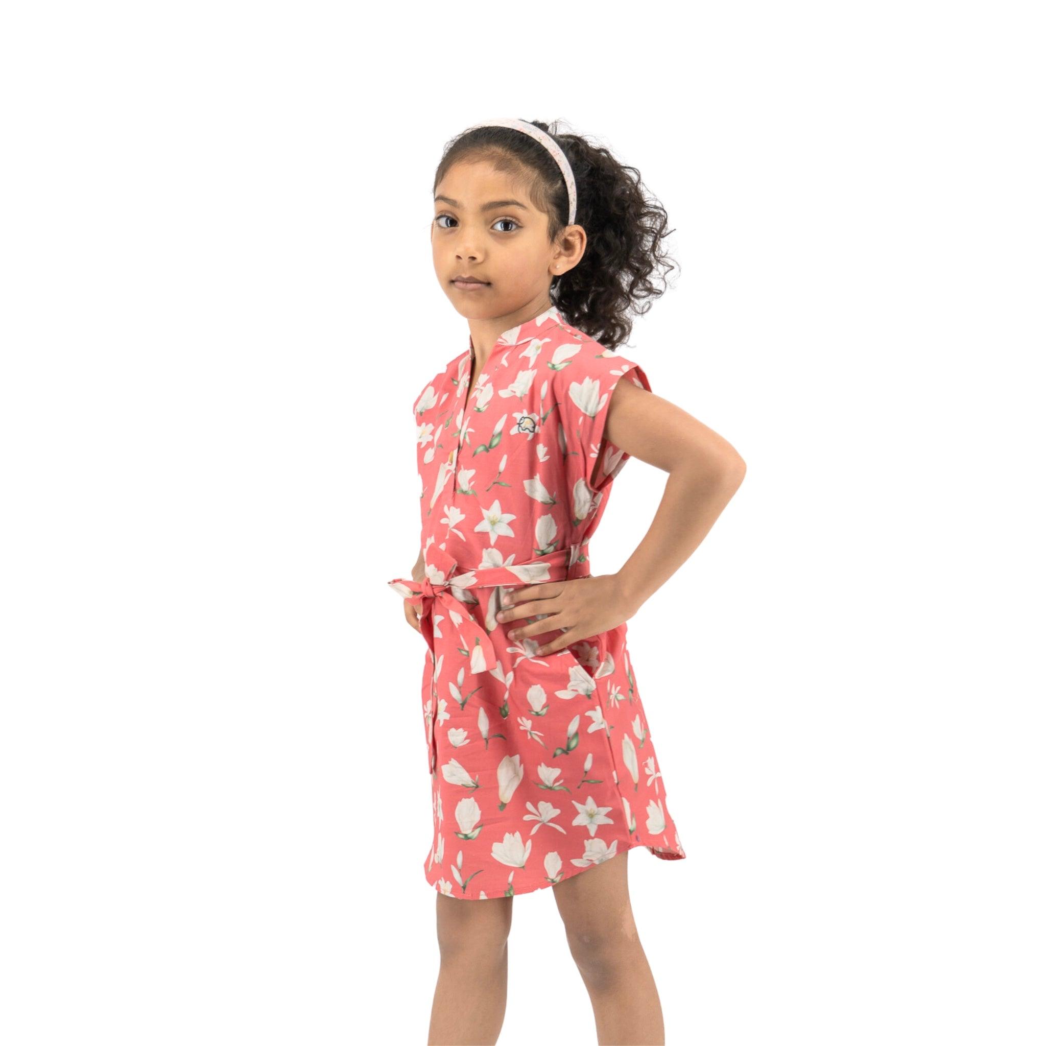 A young girl in a Mineral Red Lilly Blossom Cotton Shirt Dress from Karee stands sideways, looking at the camera, hands on her hips.