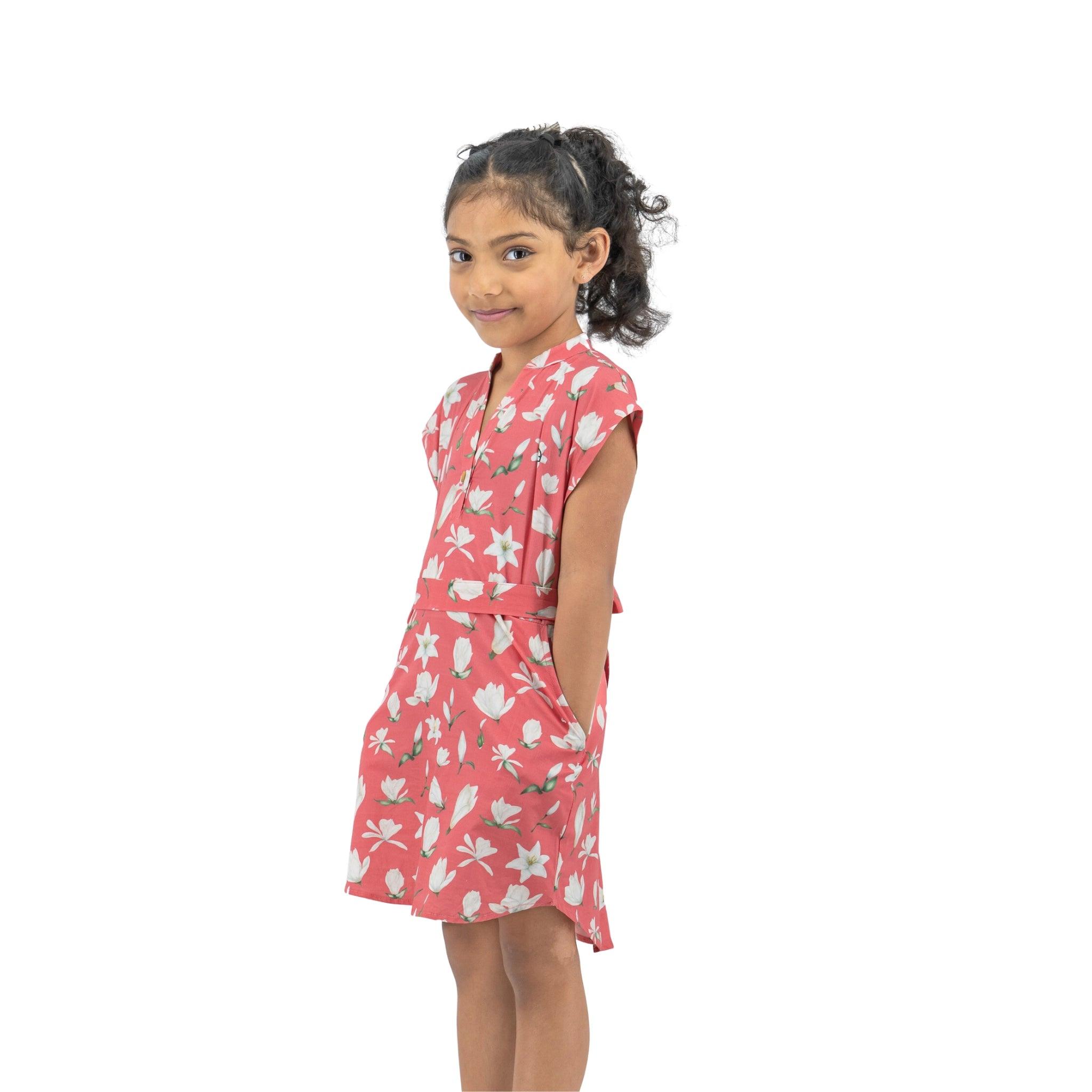 Young girl wearing a Karee Mineral Red Lilly Blossom Cotton Shirt Dress, standing sideways and looking over her shoulder with a smile, isolated on a white background.