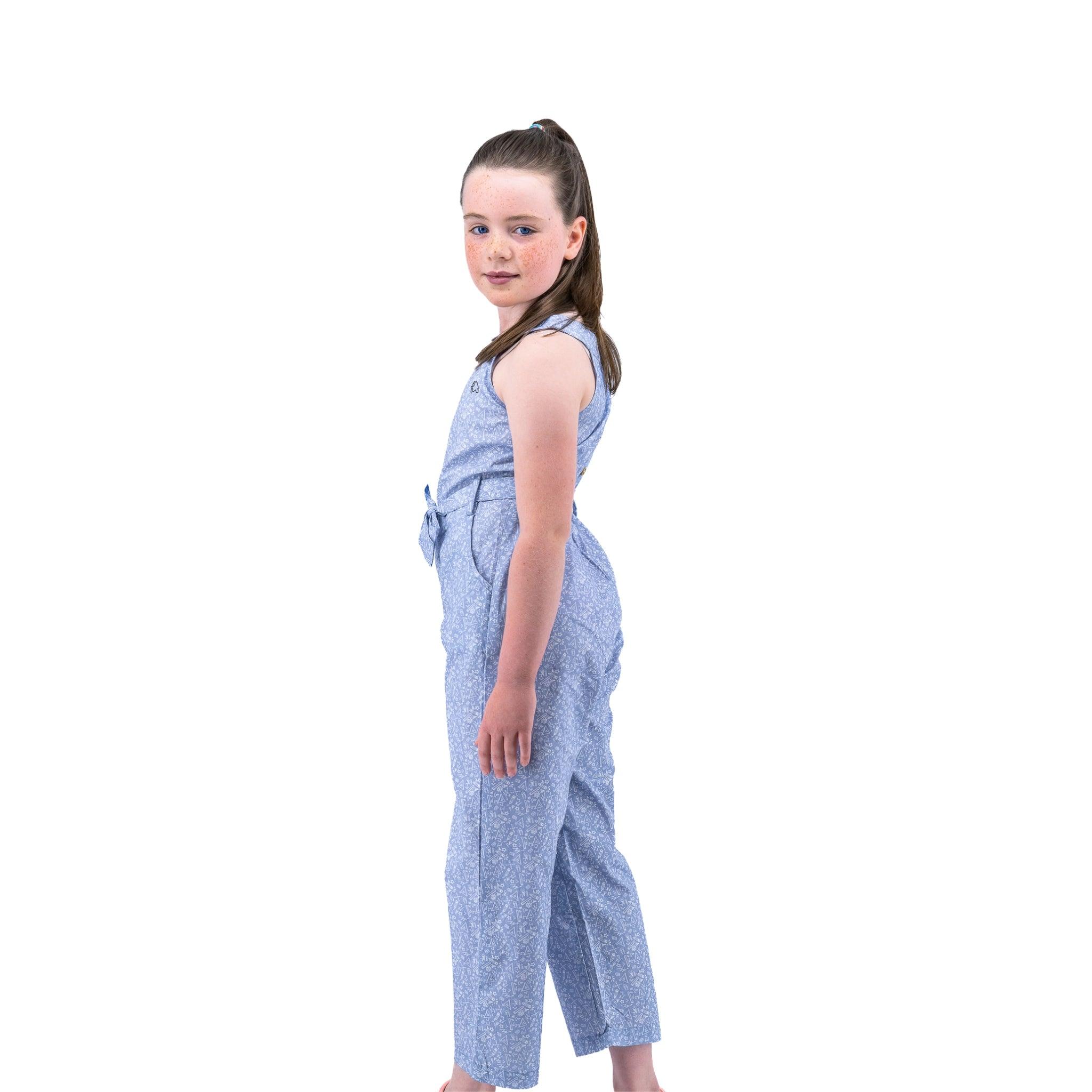 A young girl wearing a Karee Purple Impression Cotton Jumpsuit for kids stands sideways and looks over her shoulder against a white background.